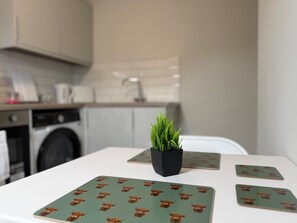 A kitchen with a table set with four square placemats featuring a pattern of brown animals, a small potted plant, and a white countertop. - Walk to Train Bolton ~Free Parking ~close to Shops (Farnworth)