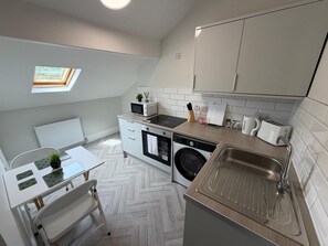 A compact kitchen with a washing machine, microwave, and sink. - Walk to Train Bolton ~Free Parking ~close to Shops (Farnworth)