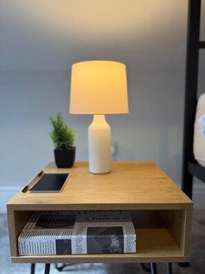 A bedside table with a lamp, a smartphone, a notebook, a potted plant, and a newspaper. - Walk to Train Bolton ~Free Parking ~close to Shops (Farnworth)