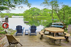 Um deck de madeira com cadeiras Adirondack, uma mesa de piquenique e um flutuador.