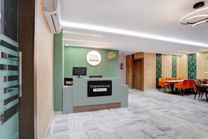 A reception area with a sign reading 'TOWN HOUSE' and a 'TOWNHOUSE OYO-Serviced' sign. There is a reception desk, a television, and a fire extinguisher on the wall. - Classic Prayagraj New Cantt (Prayagraj)