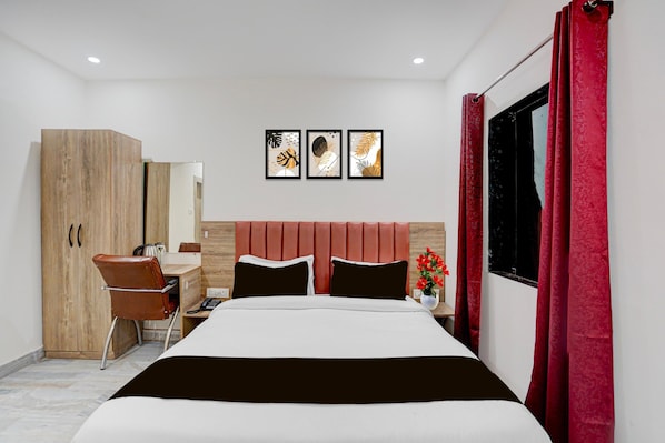 A hotel room with a bed, a desk, a chair, a wardrobe, and three framed pictures on the wall.