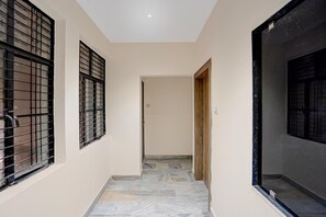 A corridor with tiled flooring, a wooden door, and barred windows. - Classic Prayagraj New Cantt (Prayagraj)