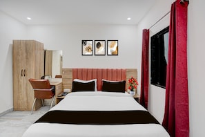 A hotel room with a bed, a desk, a chair, a wardrobe, and three framed pictures on the wall.