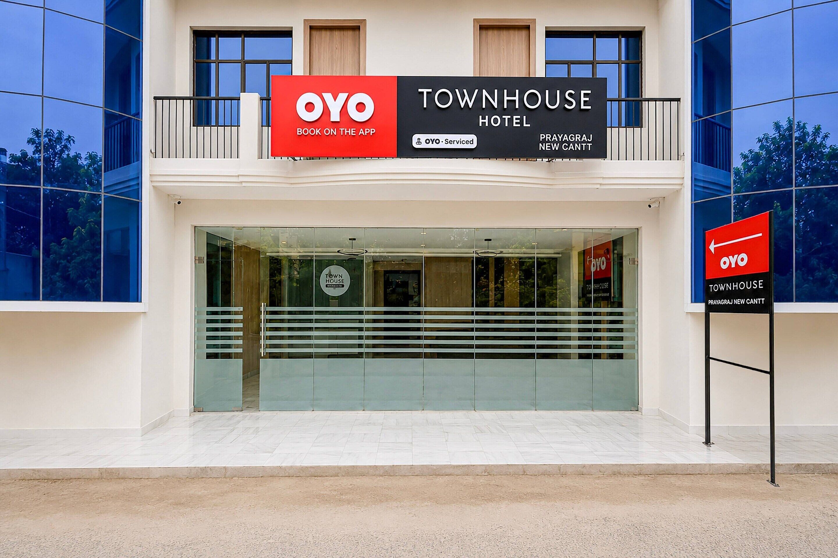 A modern building with a large glass entrance, a prominent OYO Townhouse Hotel sign, and a sign indicating the location as Prayagraj New Cantt.
