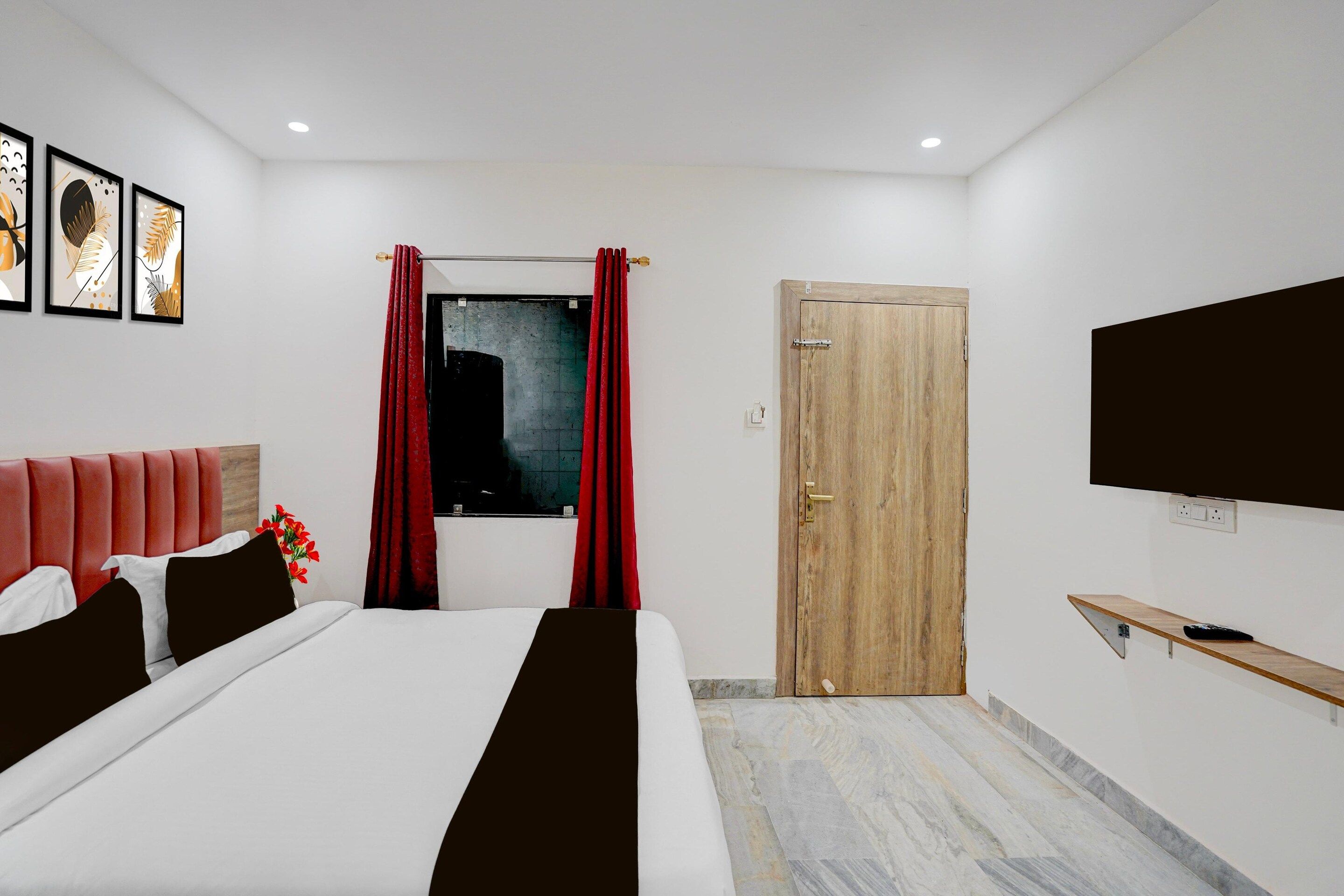 A modern hotel room with a bed, a TV, a wooden door, and a window with red curtains.