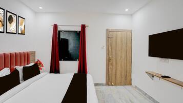A modern hotel room with a bed, a TV, a wooden door, and a window with red curtains.