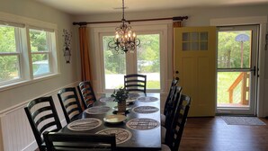 A dining room with a table set for six, surrounded by chairs, a chandelier, and a view through a door to a deck. - A 3-bedroom mountain retreat perfect for families, friends, and every adventure! (Zirconia)