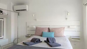 Habitación de hotel con cama, almohadas, mesita de noche, aire acondicionado y ventana.
