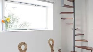 Una habitación con ventana, estante en la pared y dos sillones de mimbre.