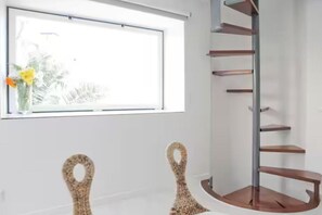 Ein Zimmer mit Fenster, einer Wandablage und zwei Korbstühlen.