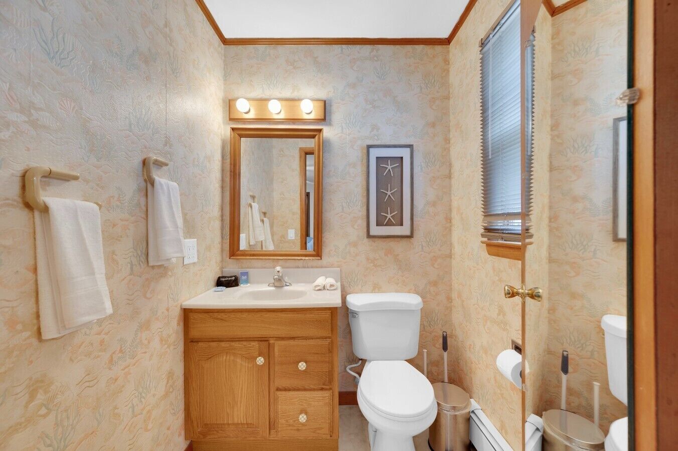 Ein Badezimmer mit einem Holz-Waschtisch, einer Toilette, einem Waschbecken mit Spiegel darüber und einem gerahmten Bild an der Wand.