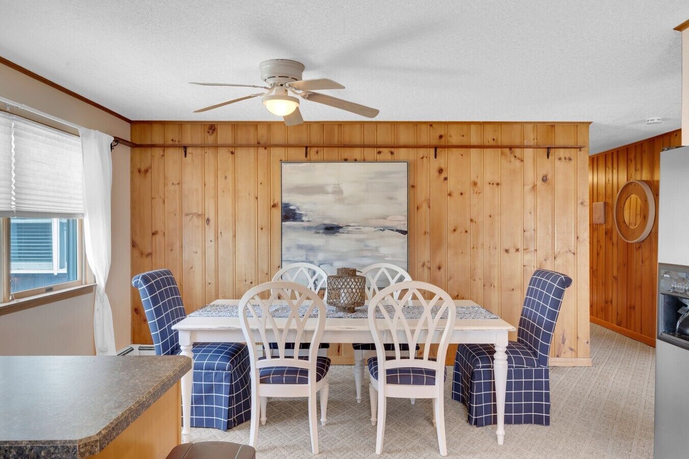 A dining area with a wooden wall, a ceiling fan, and a large painting.