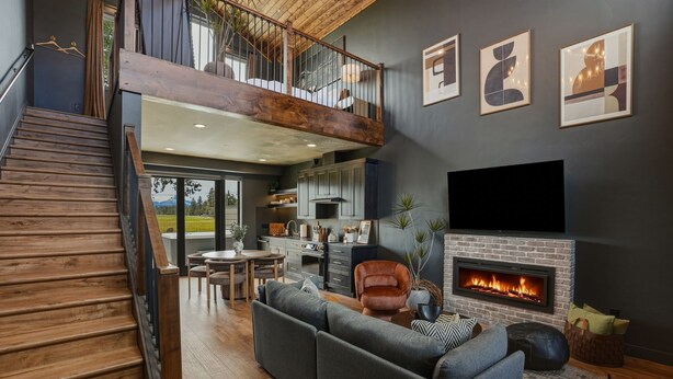A modern living room with a fireplace, a sofa, a dining area, and a staircase leading to a loft.