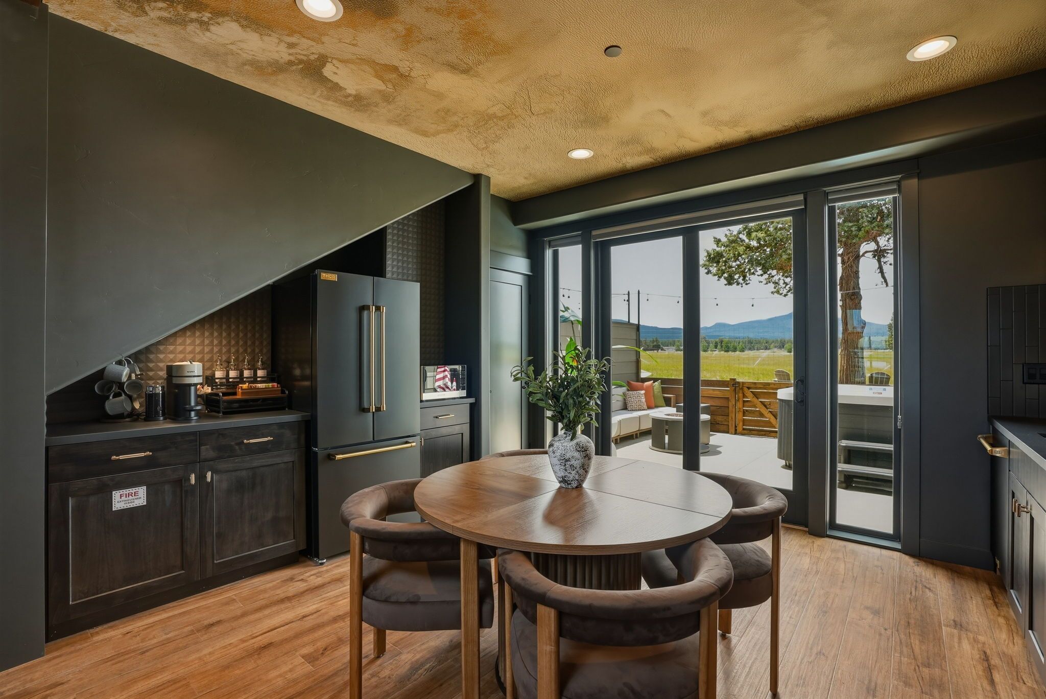 A modern kitchen with dark cabinetry, a round wooden table, and a view of a patio with outdoor seating.