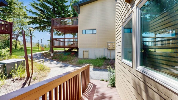 Un bâtiment à deux étages doté d’une terrasse en bois, d’un petit espace extérieur avec un banc et d’une grande fenêtre.