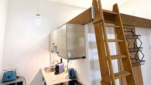Une cuisine compacte équipée d’un four à micro-ondes, d’un grille-pain et d’une bouilloire, ainsi que d’une échelle en bois et d’un étendoir suspendu.