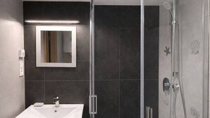 Une salle de bain moderne avec une douche à parois de verre, un meuble-lavabo avec un miroir et des murs recouverts de carreaux foncés.