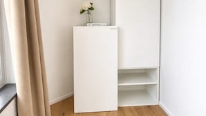 A corner of a room with a white cabinet, a small table with a vase of flowers, and a window with curtains. - Sleek & Modern New Build Flat (Prague)