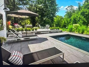 A swimming pool area with lounge chairs and a table, surrounded by greenery.