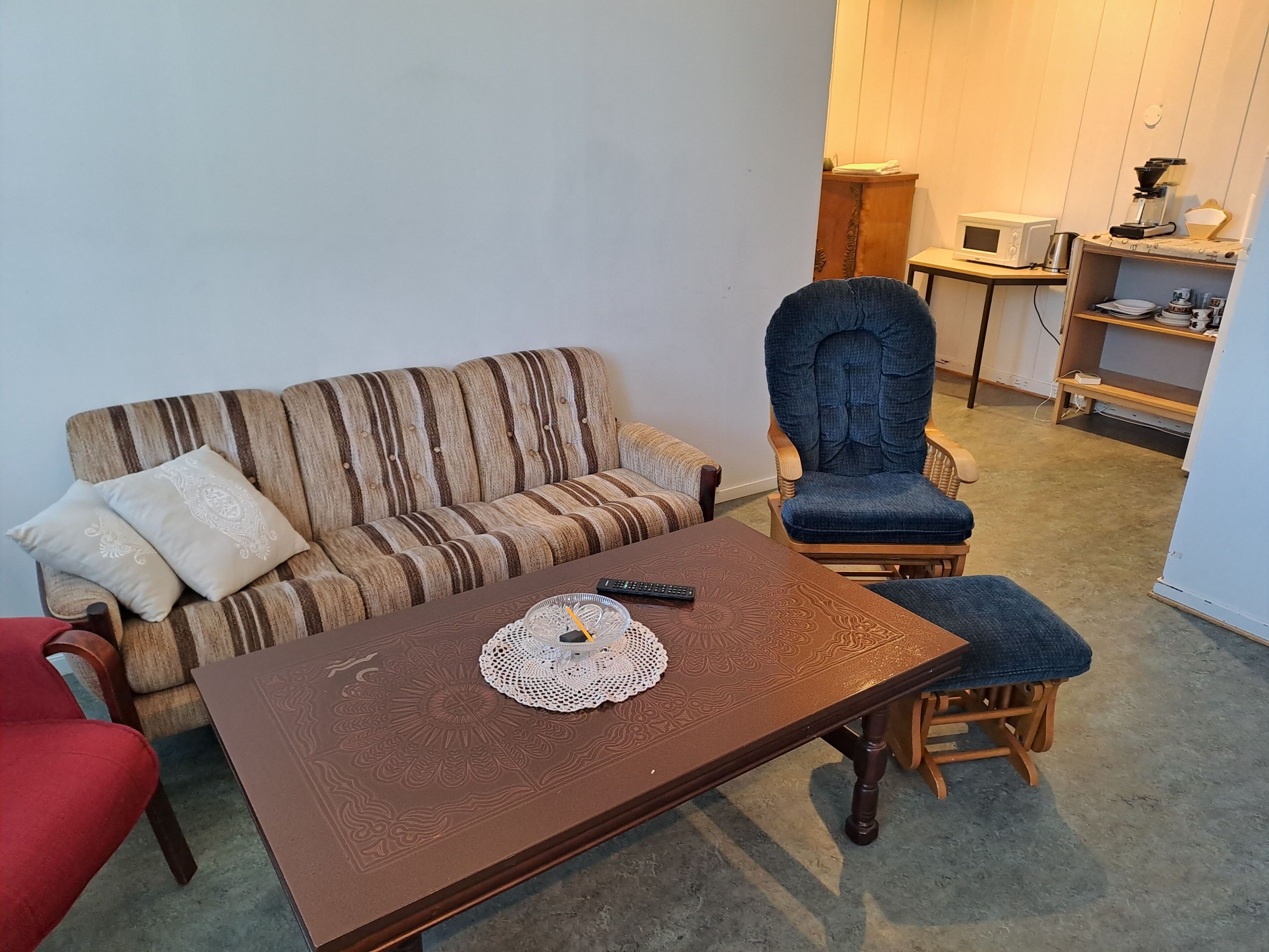 Een woonkamer met een gestreepte bank, een blauwe fauteuil, een houten salontafel en een bijzettafeltje met een magnetron.