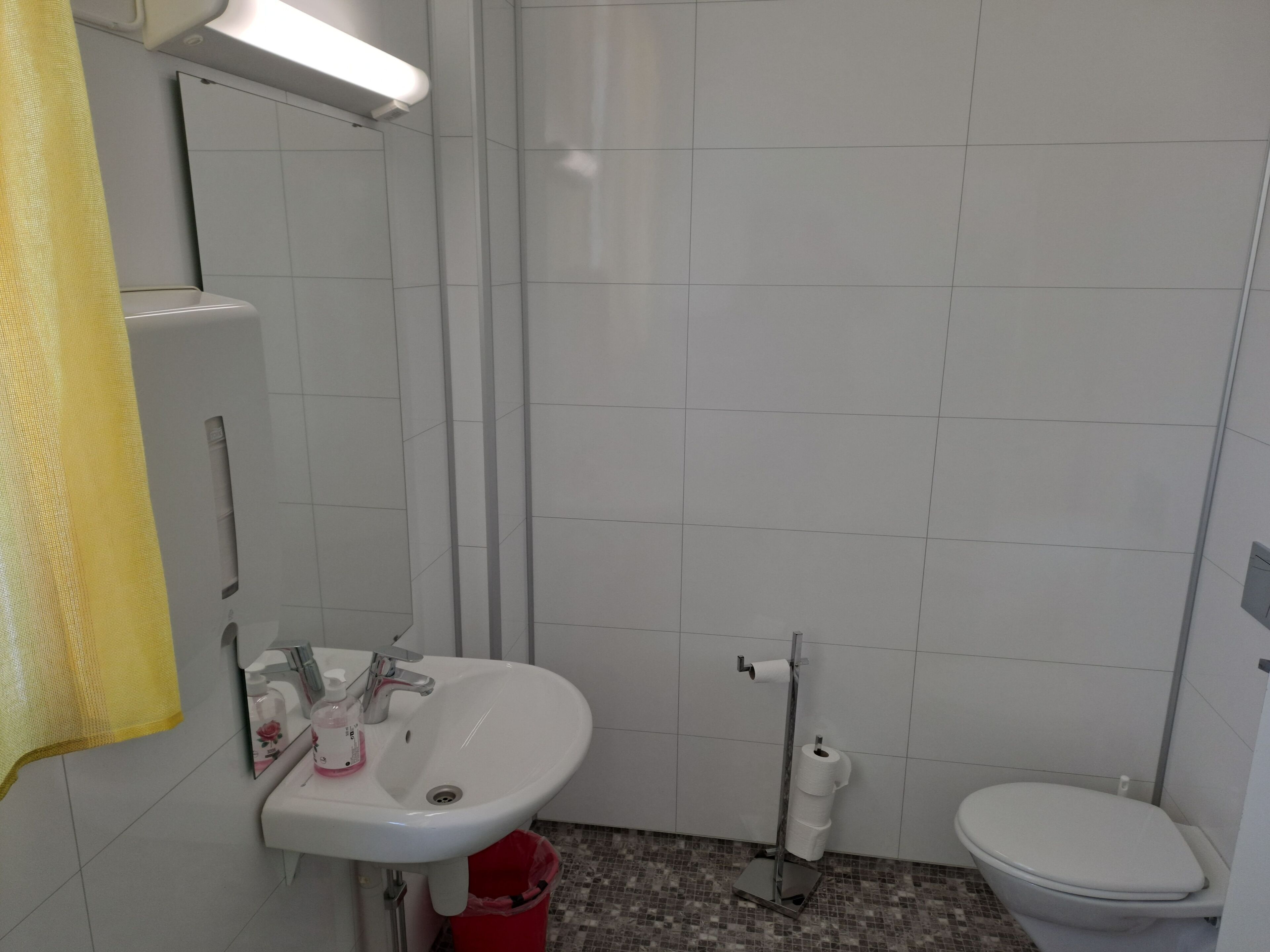 Un baño con lavamanos blanco, inodoro y un cubo de basura rojo.