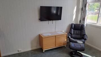 A room with a flat-screen TV mounted on the wall, a wooden cabinet with papers, a leather chair, and a window with curtains.