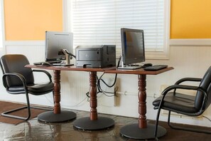 Ein Computertisch mit Drucker, zwei Monitoren und Tastatur. Zwei schwarze Bürostühle mit Rollen.