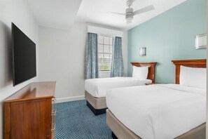 Ein Hotelzimmer mit zwei Betten, einem Flachbildfernseher, einem Deckenventilator und einem Fenster mit Vorhängen.