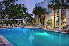 A swimming pool with lounge chairs and umbrellas, surrounded by palm trees and a modern building. - Marathon Waterfront Stay | Outdoor Pool | Pets Are Allowed (Marathon)