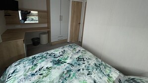 A bedroom with a bed, a wardrobe, a small window, and a desk area. - Rockley Park (Poole)