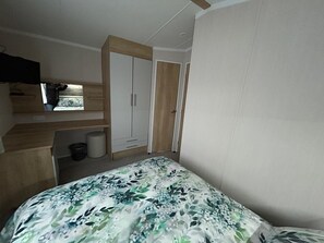 A bedroom with a bed, a wardrobe, a small window, and a desk area. - Rockley Park (Poole)