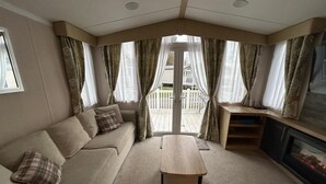 A cozy living room with a sofa, a coffee table, a fireplace, and a view of a deck. - Rockley Park (Poole)