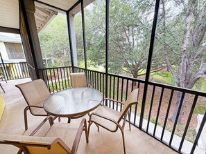 Ein Balkon mit Glastisch und Stühlen, Blick auf Bäume und ein Gebäude im Hintergrund.