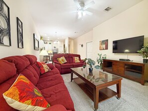 Ein Wohnzimmer mit Ecksofa, Couchtisch, Fernseher und Deckenventilator.