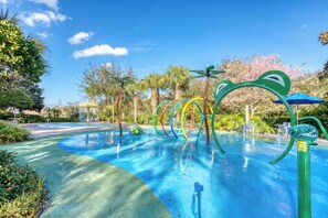 Ein Schwimmbecken mit bunten Wasserspielen und Palmen im Hintergrund.