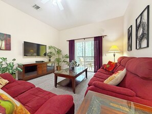 A living room with a red sofa, a TV, a wooden cabinet, and a balcony with curtains. - Bright resort condo with private balcony - Bahama Bay (Davenport)