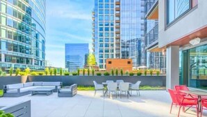 Una terraza en la azotea con mobiliario exterior, un edificio pequeño y rascacielos al fondo.