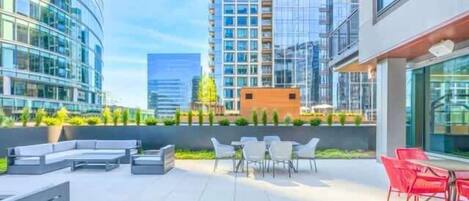 A rooftop patio with outdoor seating, a small building, and high-rise buildings in the background.