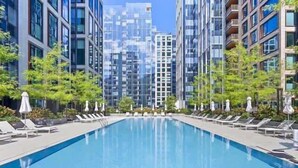 Una piscina con sillones de descanso y sombrillas, rodeada de edificios modernos.