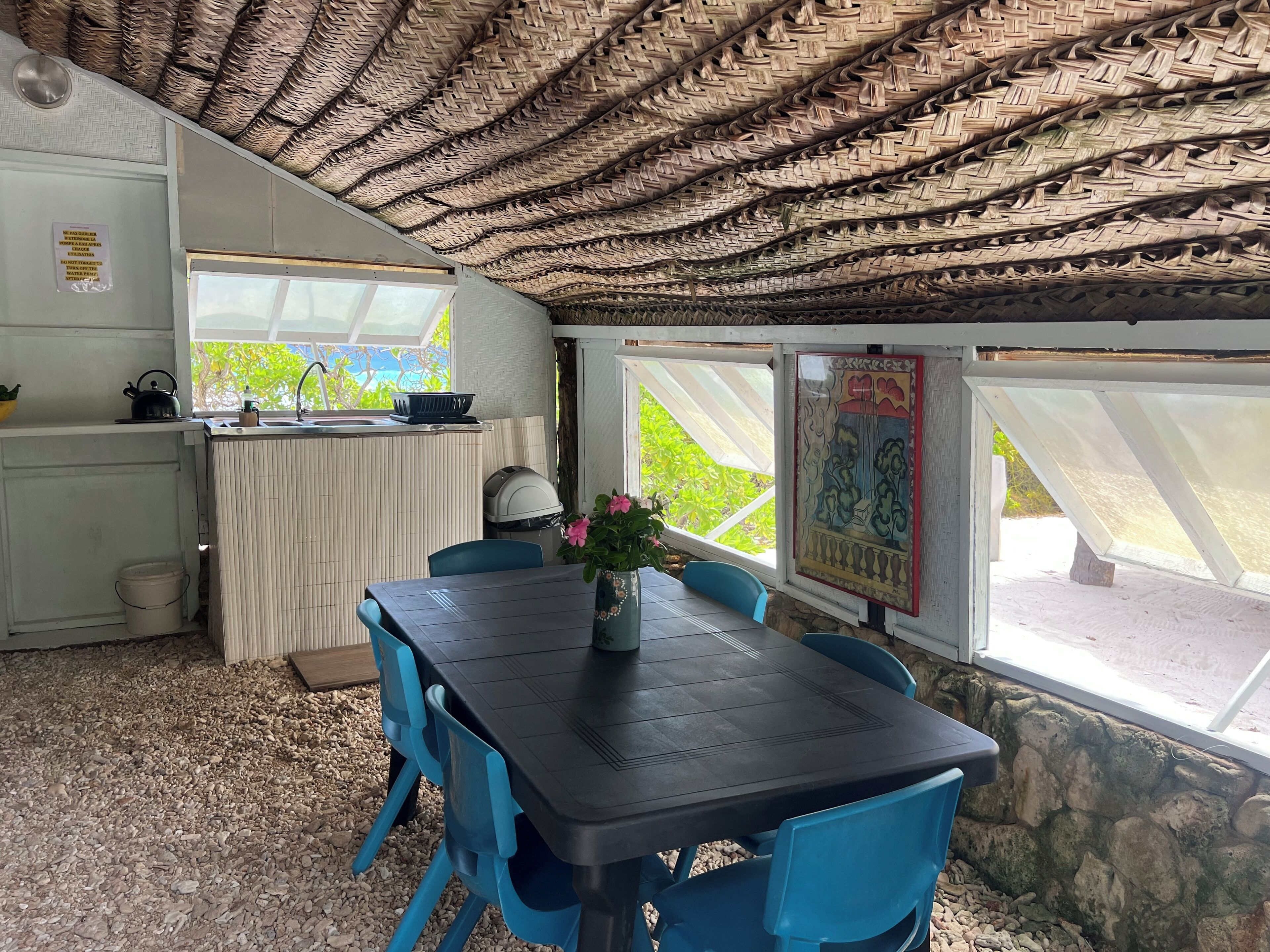 Une pièce avec un plafond en osier, une table avec des chaises, une fenêtre donnant sur un paysage agréable et un coin cuisine équipé d’une bouilloire et d’un saladier.
