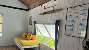 A room with a bed, a window, a wall-mounted fan, and a framed fish illustration. - Fare Miki Miki (Huahine)