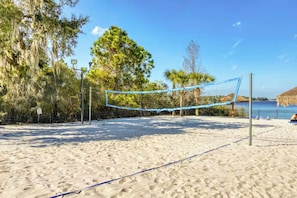 Un terrain de beach-volley avec un filet, entouré de sable et d’arbres.