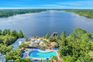 Ein Resort mit Schwimmbad, umgeben von Palmen und Liegestühlen, mit Blick auf ein großes Gewässer.