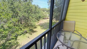 Un balcón con una mesa y sillas de vidrio, con vista a un paisaje verde con árboles.