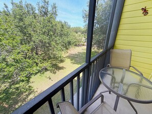 Ein Balkon mit Glastisch und Stühlen, der auf eine grüne Landschaft mit Bäumen blickt.