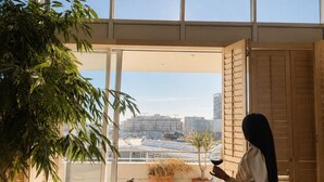Ein modernes Wohnzimmer mit einem großen Fenster, einem Blumentopf, einem Ledersofa und einer Person, die am Fenster steht.