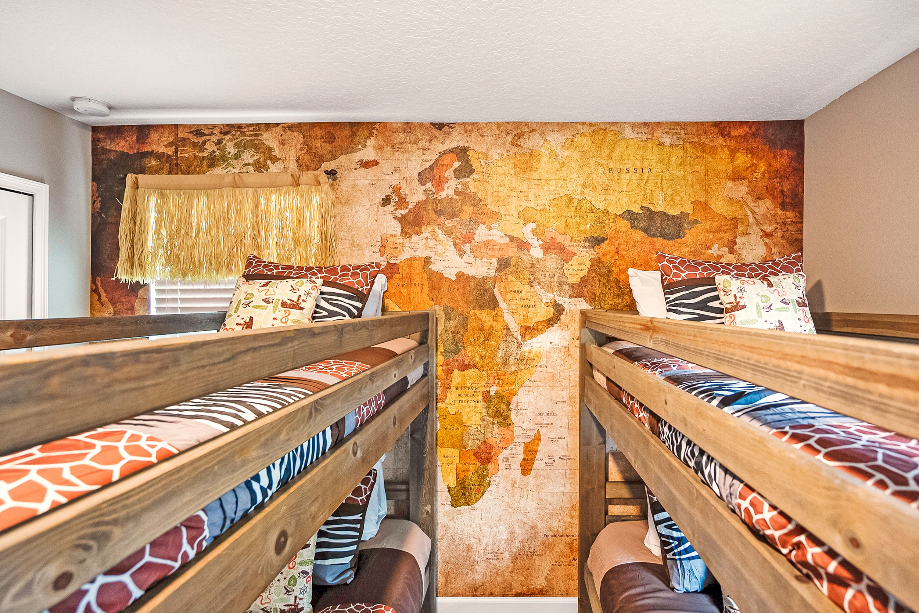 Une chambre avec des lits superposés, une fresque représentant une carte du monde et une fenêtre avec un rideau.