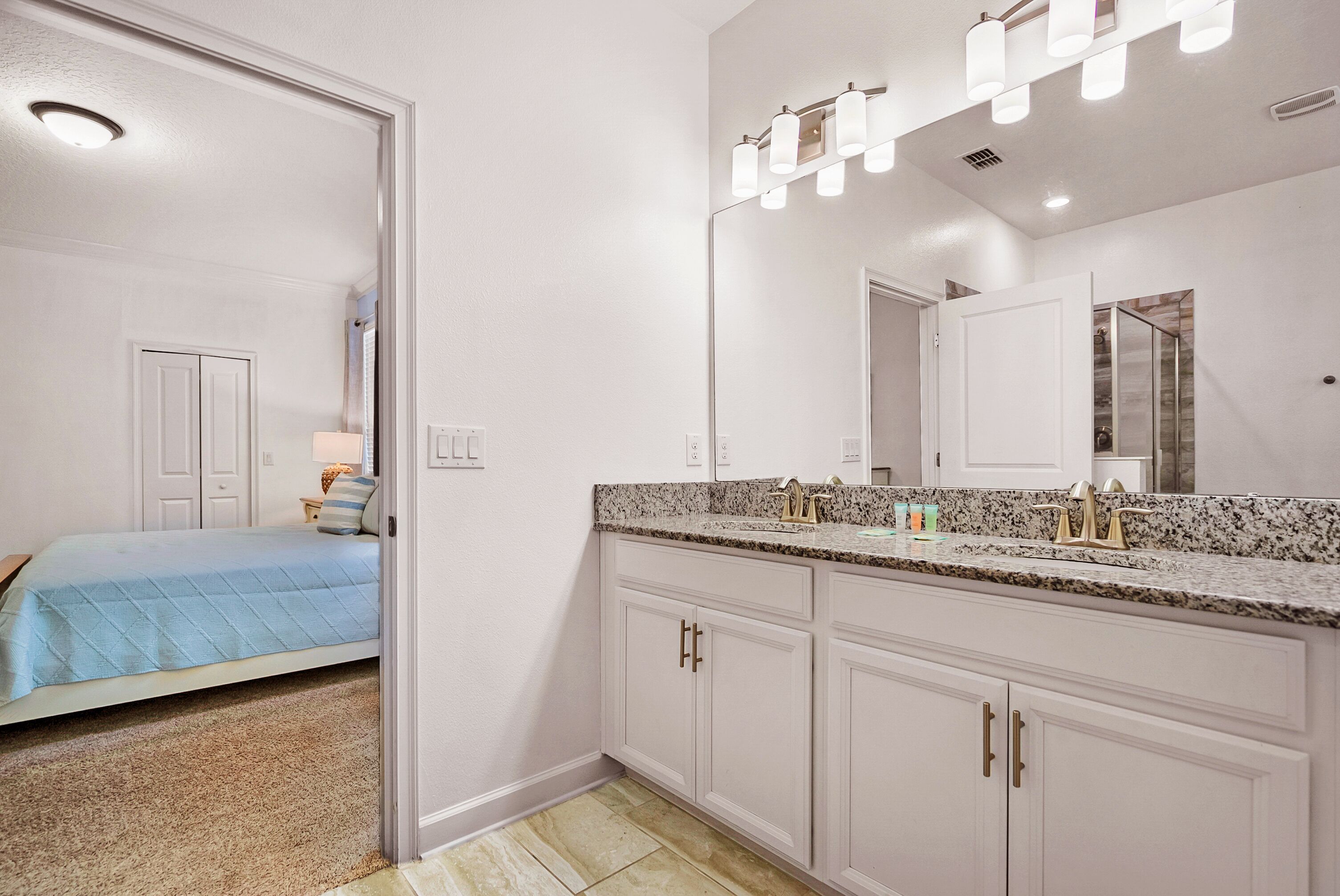 A bathroom with a large mirror, a granite countertop, and a walk-in closet.
