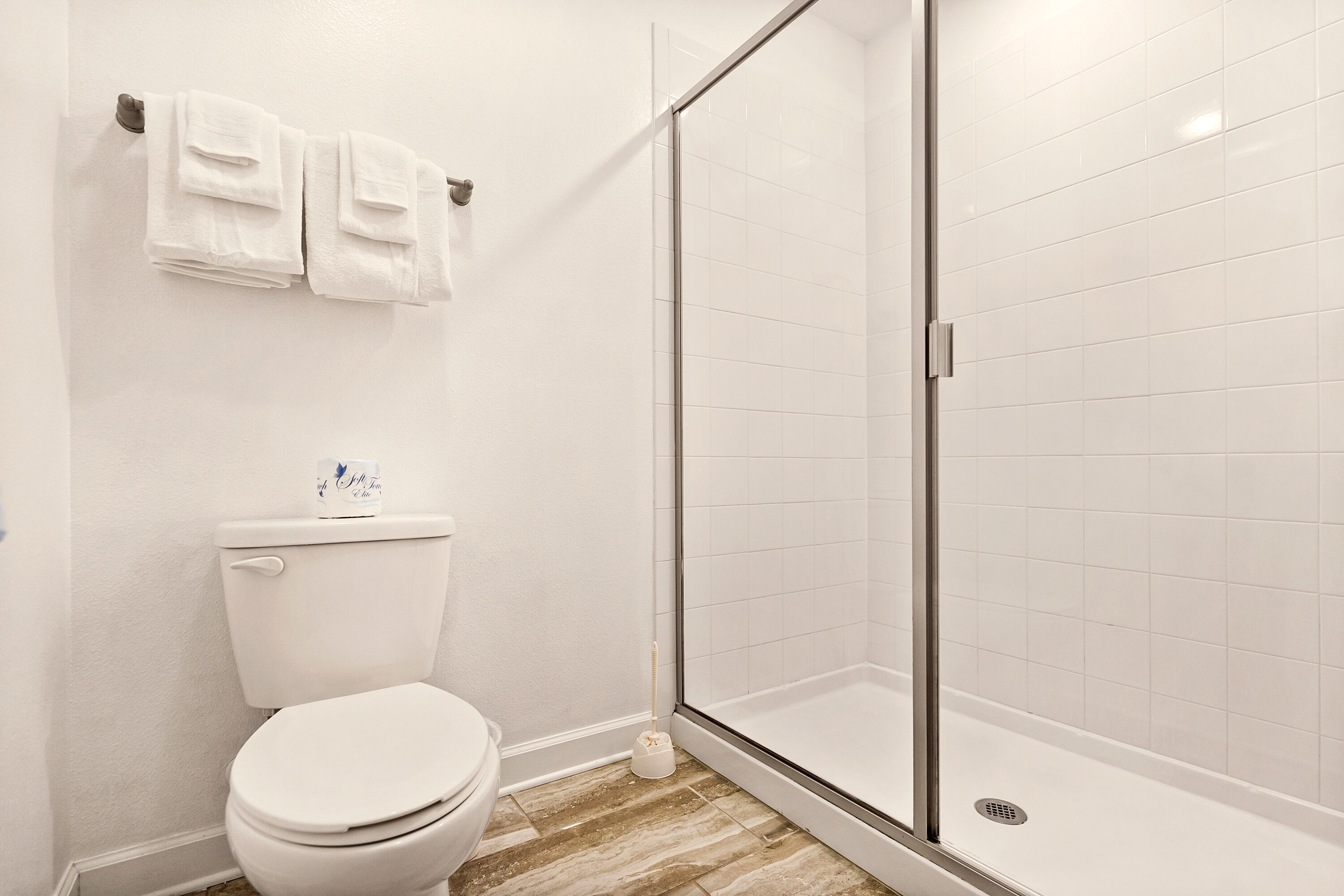 A bathroom with a toilet, a glass-enclosed shower, and a towel rack with two towels.